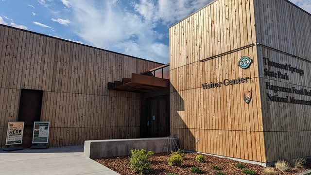 The entrance to a boxy, wood-paneled visitor center, with the NPS and Idaho State Parks logos.