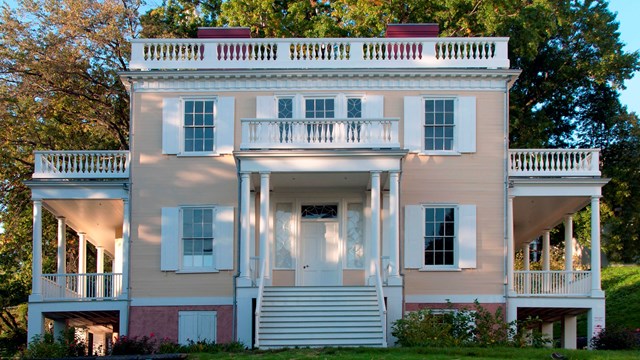 Hamilton Grange, a yellow, symmetrical house, sits atop a hill.