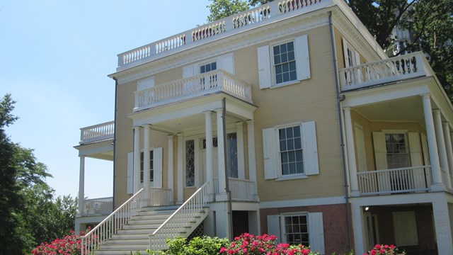 A yellow house stands among rose bushes.