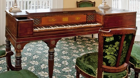 A late 18th century model pianoforte stands among chairs upholstered in green silk.