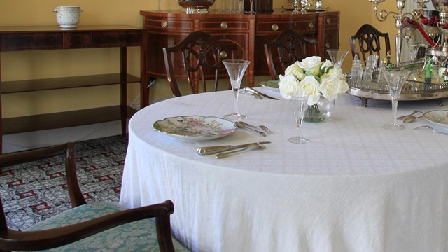 A table in a white table cloth bears silverware, a mirror tray, candle sticks, flowers and glasses.