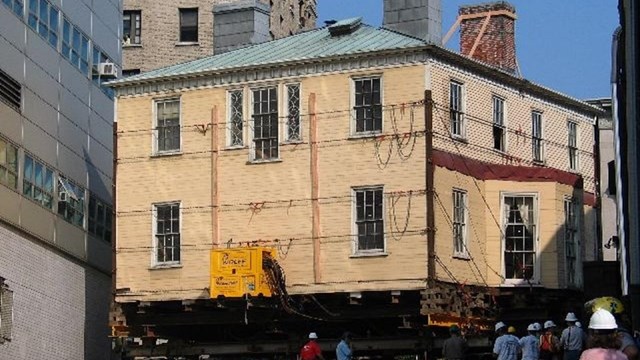 A large yellow house, propped up on dollies, rolling down a city street.