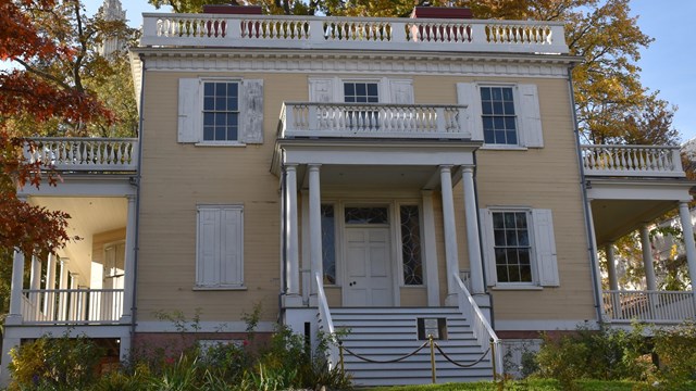 A yellow house standing stately among fall-colored foliage.