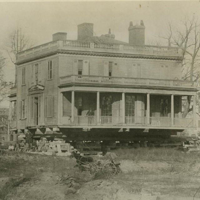 A house stands on a bare hill on planks, ready to be moved.