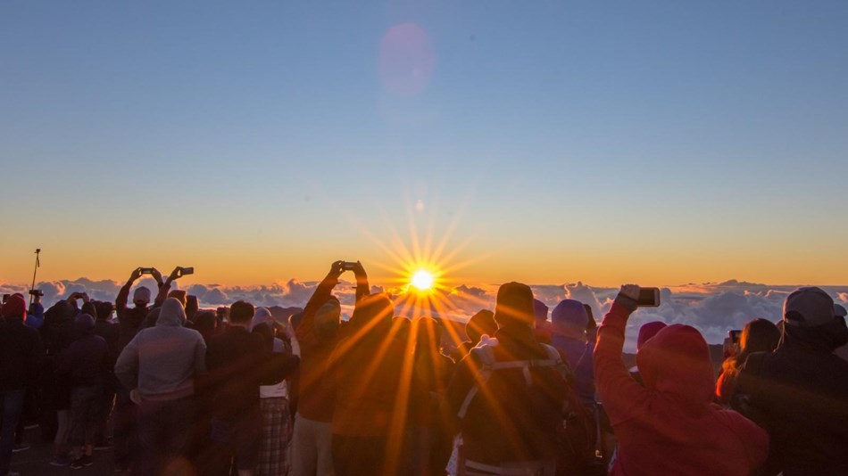 A crowd of visitors watches sunrise from the visitor center.