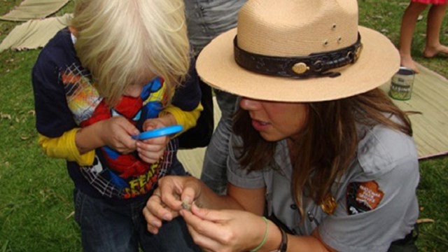 A ranger and a student look through a magnifying glass.