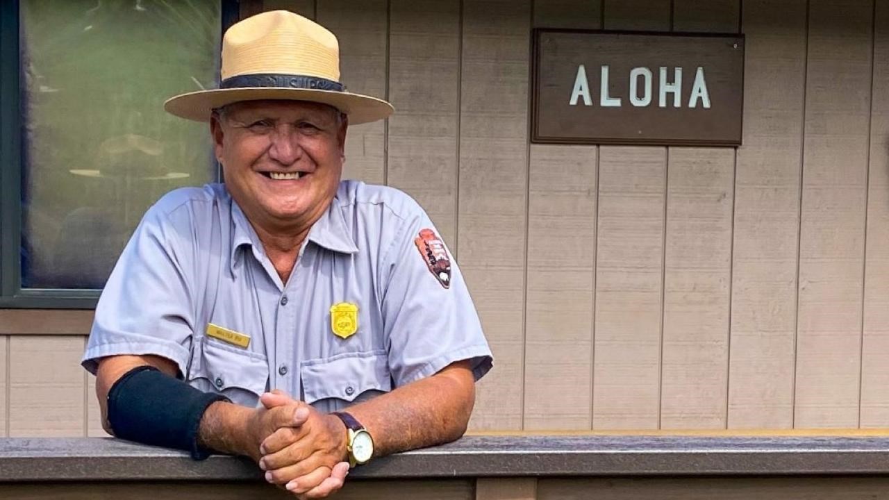 ranger leans over railing with an "aloha" sign behind them