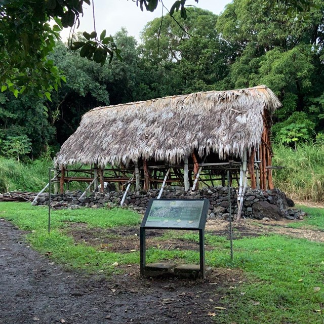 A traditional open air Hawaiian building stands upon a lava rock foundation.