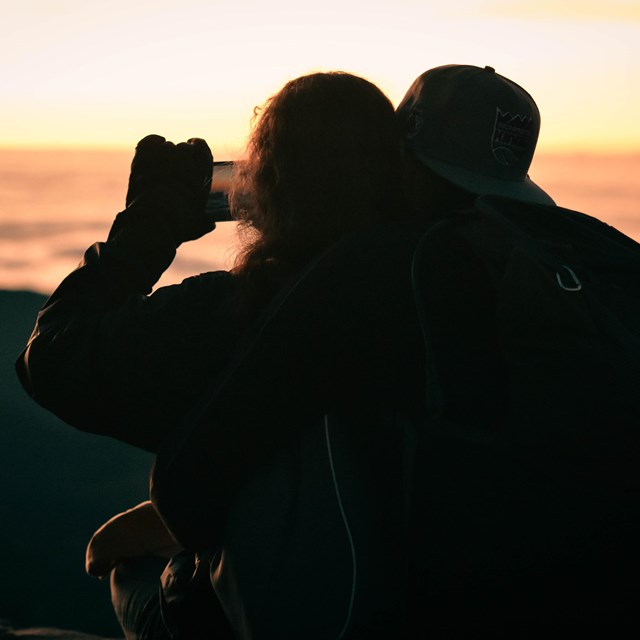 A dimmed horizon with pink and orange colors with two silhouettes of people taking a photo