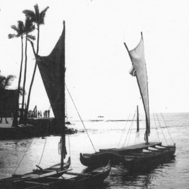 black and white image of two double-hulled canoes sit in a bay