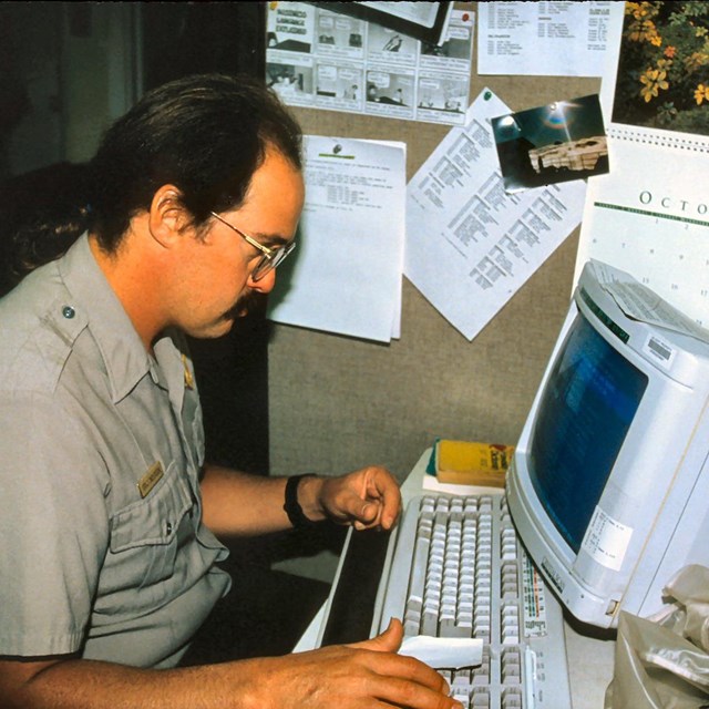 man sitting at a desk looking at a computer. 