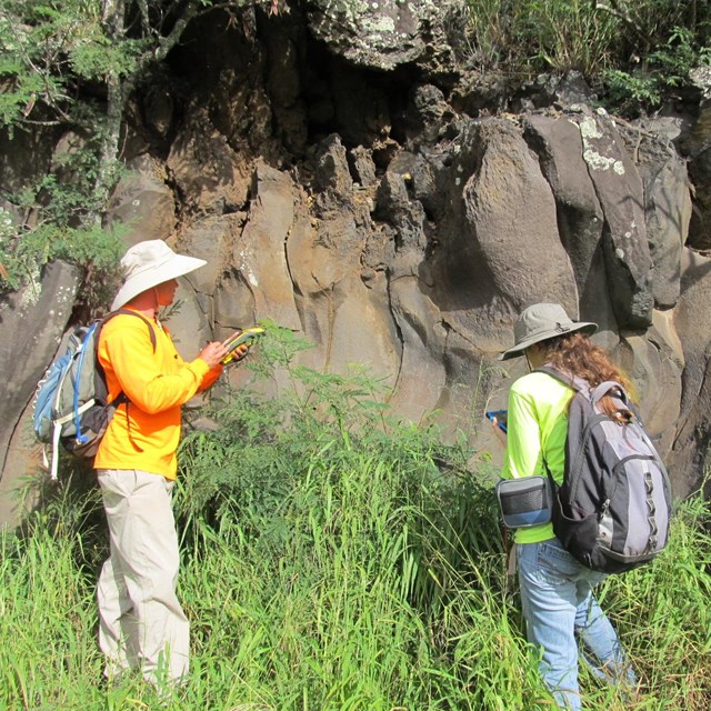 Two people stand in the grass looking at a rocky, archeological site.