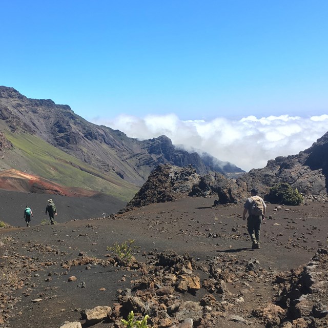 Three hikers walk along a trail with colorful cinder cones ahead of them.