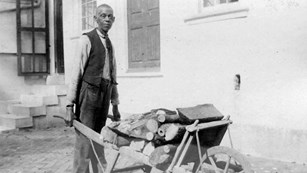 Enslaved black man with wheelbarrow outside of slave quarters