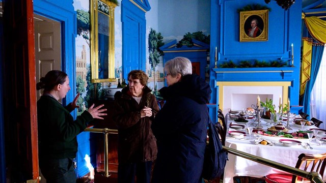 Ranger talking with visitors in mansion dining room.
