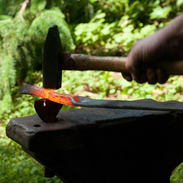 A hammer striking a piece of hot iron on an anvil.