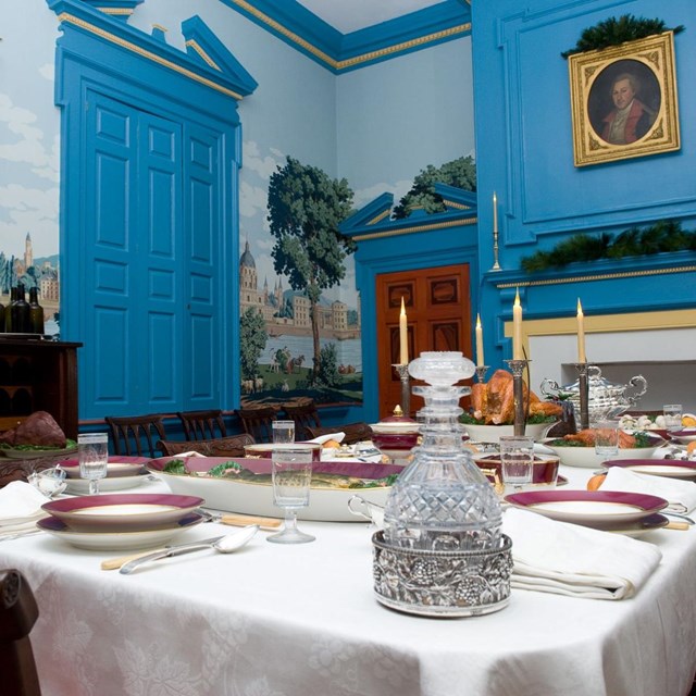 Dining room table with expensive setting.  Blue wallpaper in background.