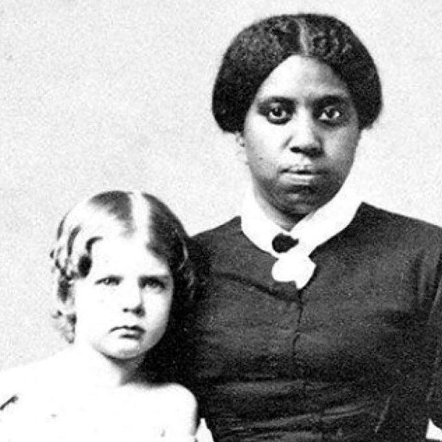A black and white photo of an enslaved person with a white child.