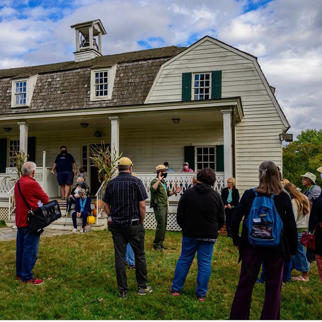 A ranger leads a program in front of a farm house.