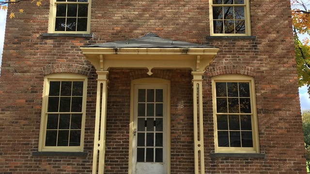 The front of a brick two-story house with small white columns in front. 