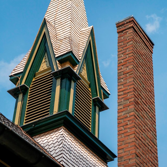A church steeple, painted in green and yellow, along with a brick chimney.