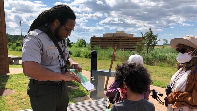A park ranger assists two guests with an activity sheet.