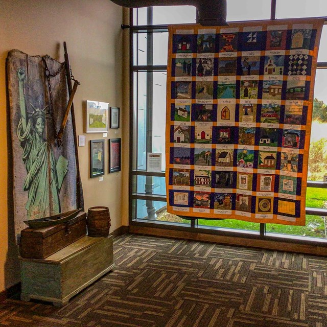 A room with an eight-foot quilt and other artwork on three walls. 