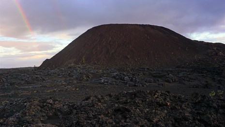 A cinder cone with a rainbow behind it