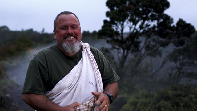 A ranger smiling holding a conch shell. 