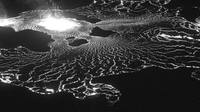 Black and white photo of molten lava at night, from above.