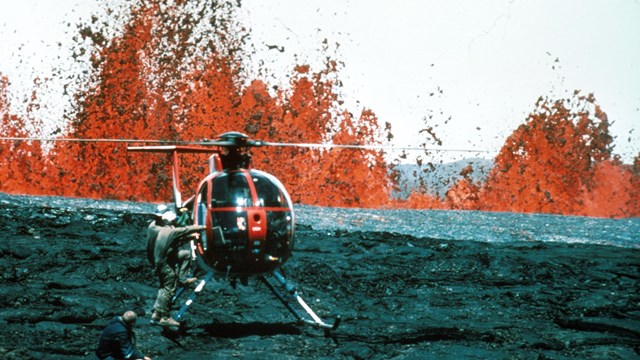 Helicopter on the ground in front fountains of orange molten lava