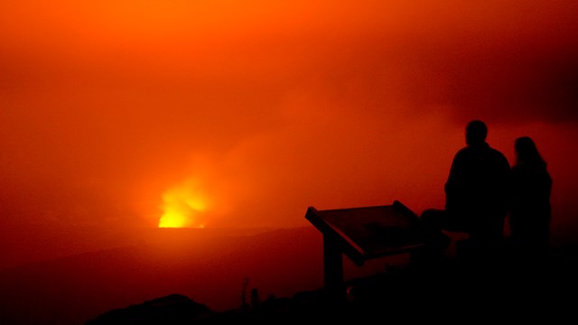 Silhouette of human figures in front of a glowing volcanic crater