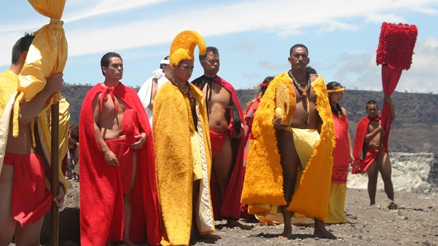 Hawaiian aliʻi and attendants all wearing red and yellow on the edge of a volcanic crater