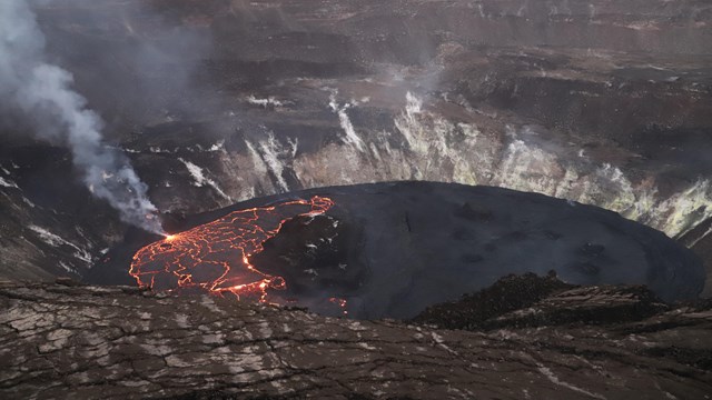 A lava lake in a volcanic crater, with half of it black and stagnant and the other half glowing 