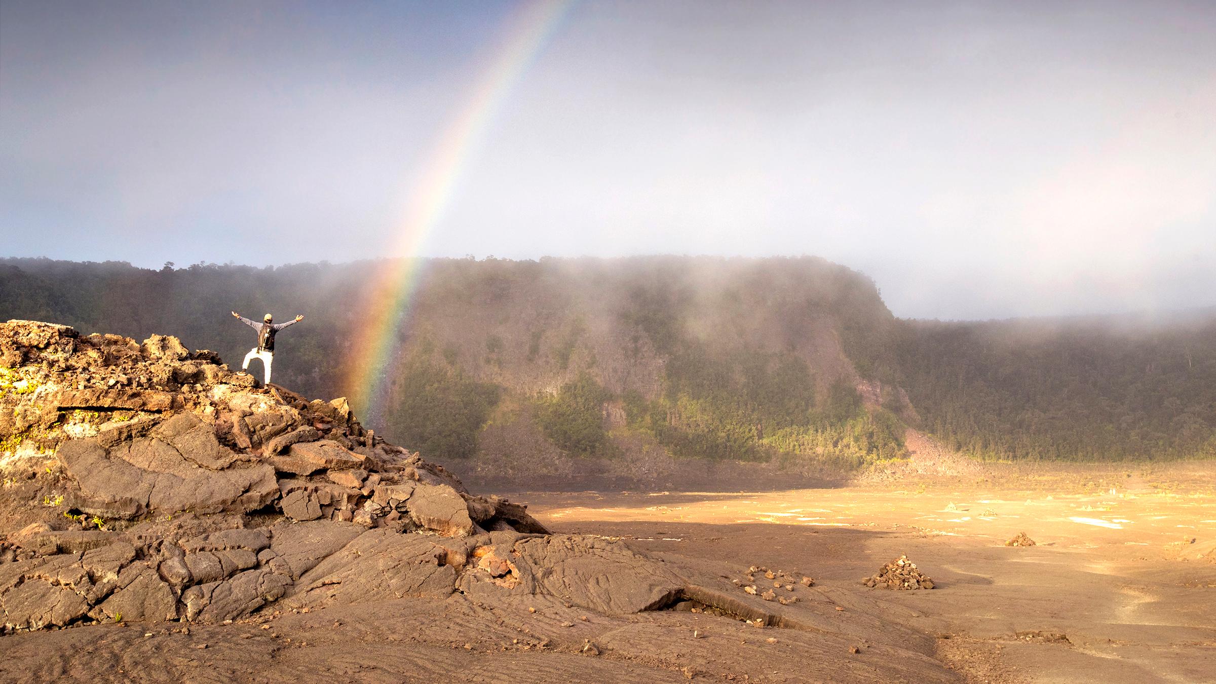 Rainbow inside a crater with a hiker in the foreground