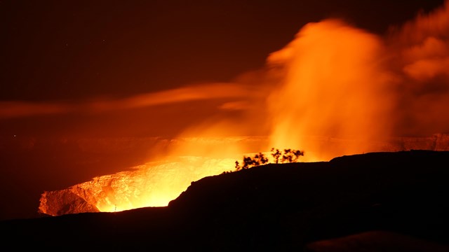 Deep dark crater at night with bright orange glow and smoke.