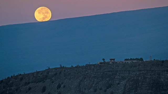 Full moon rising over a mountain ridge and building placed upon a rocky outcropping
