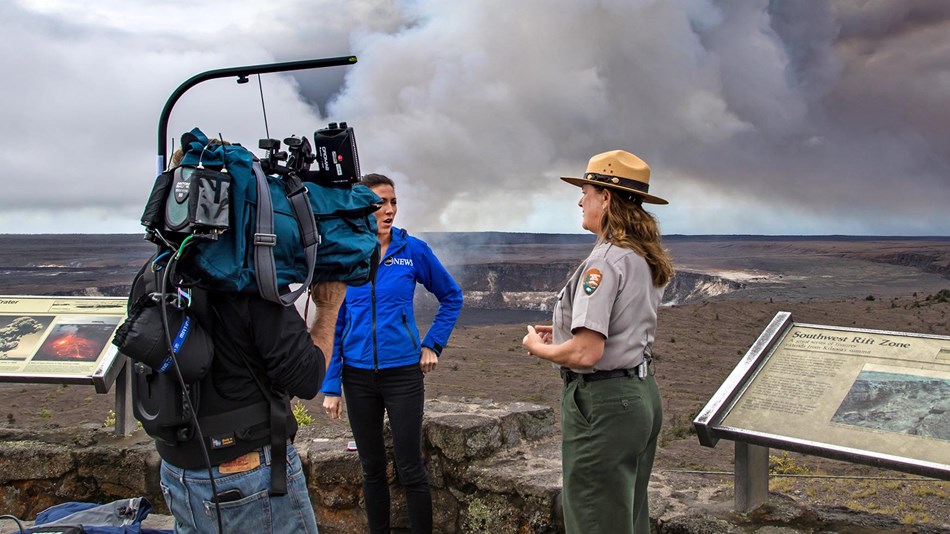 A park ranger talking to a reporter in front of an erupting volcano