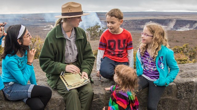 Children talking to a park ranger on a stone wall