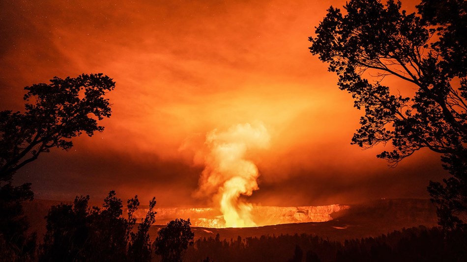 Deep dark crater at night with bright orange glow and smoke.