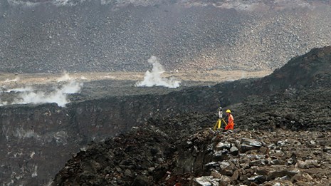 Scientist using a monitoring device atop the edge of a volcanic crater