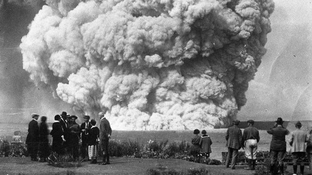 Black and white photograph of human figures in front of an ash cloud