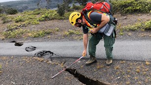Man measures large ground crack across paved trail.
