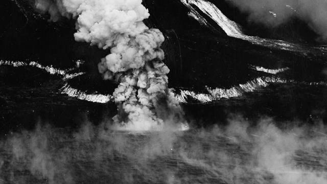 Black and white aerial photo of lava flow entering the sea