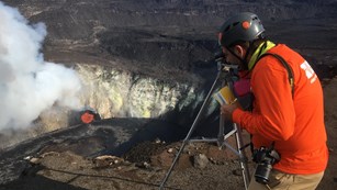 Scientist using a monitoring device atop the edge of a lava lake in a volcanic crater