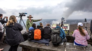 A volunteer ranger with video cameras talking to a group of people in front of a caldera