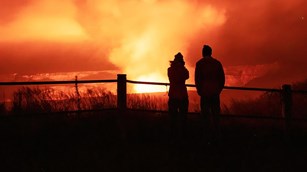 Silhouettes of park visitors watching a volcanic eruption from an overlook
