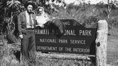 Historic photo of two people posing with park entrance sign