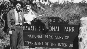 B&W photo of ranger and woman standing next to "Hawaii National Park' sign