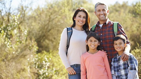 family poses for picture in a park with bushes in the background
